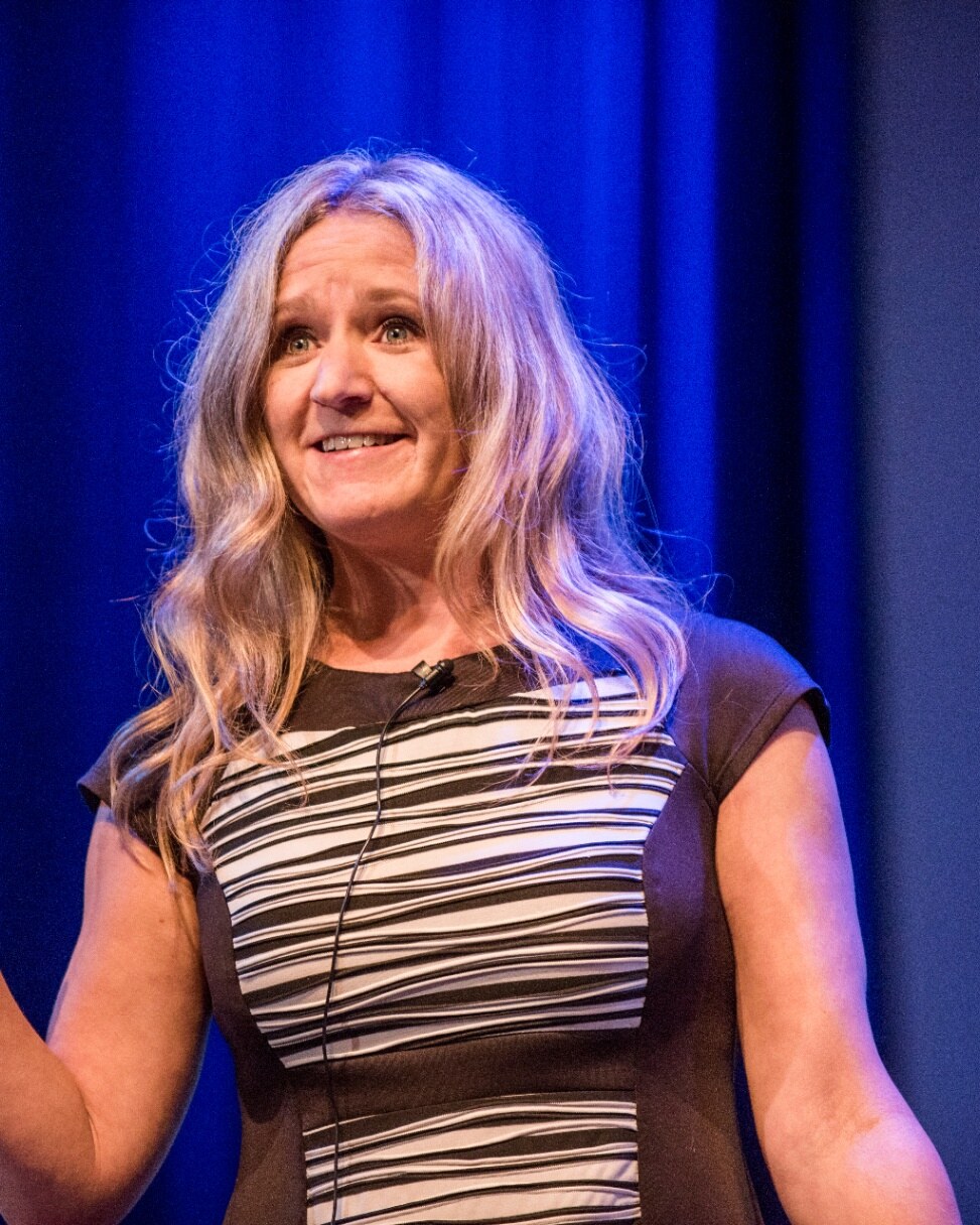 Jen DeWare speaking on stage under blue lighting
